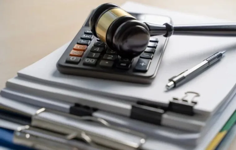 Martelo de juiz sobre uma calculadora e pilhas de documentos com clipes e caneta ao lado, representando o equilíbrio entre legislação e orçamento. A imagem simboliza a análise técnica e jurídica das características da LDO, como planejamento fiscal, definição de metas e prioridades e controle de gastos públicos. Imagem gerada por IA.